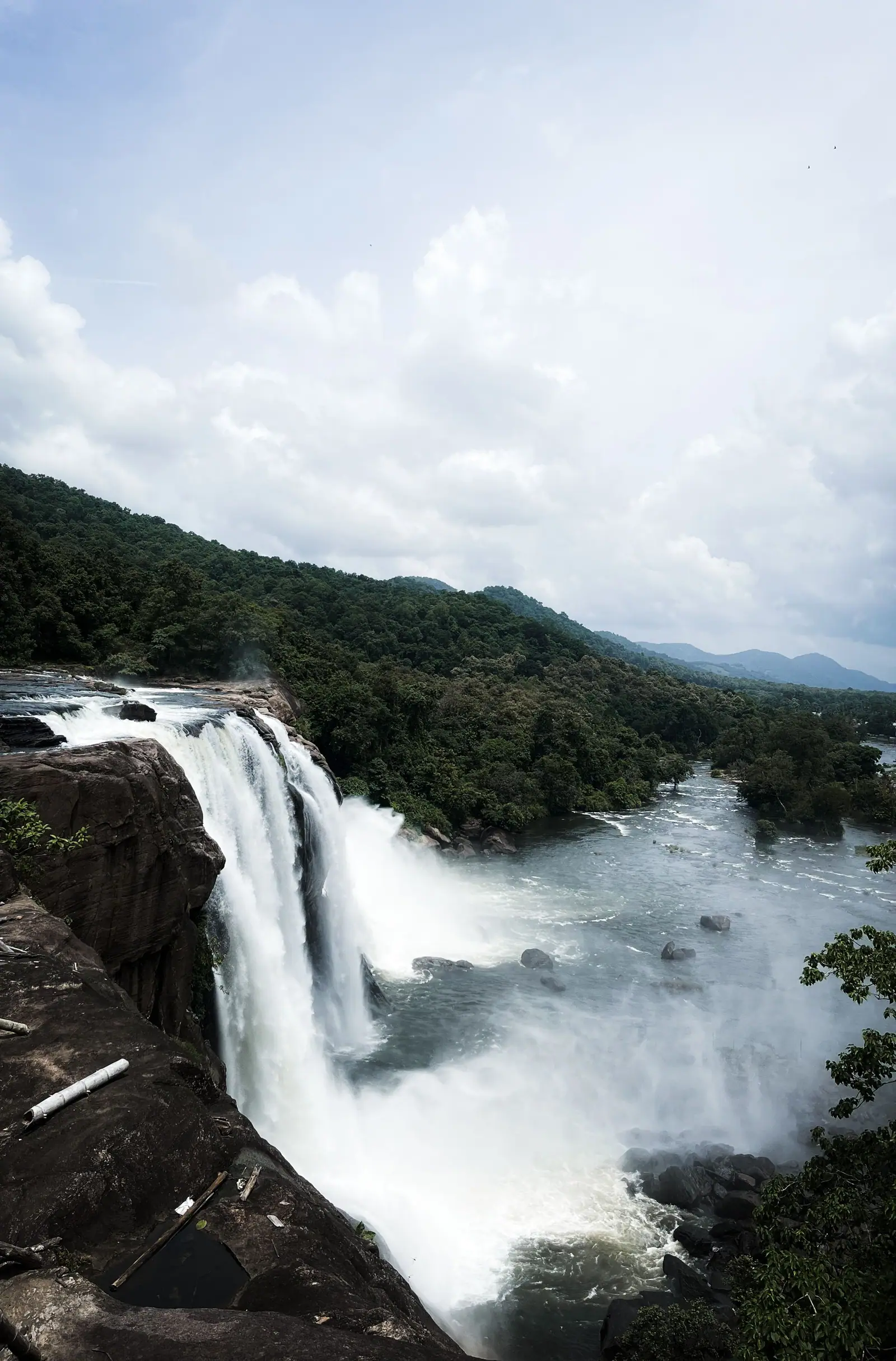 View from the top of Athirappilly Falls, with the Chalakudy river plunging over the rocky ledge into forested hills