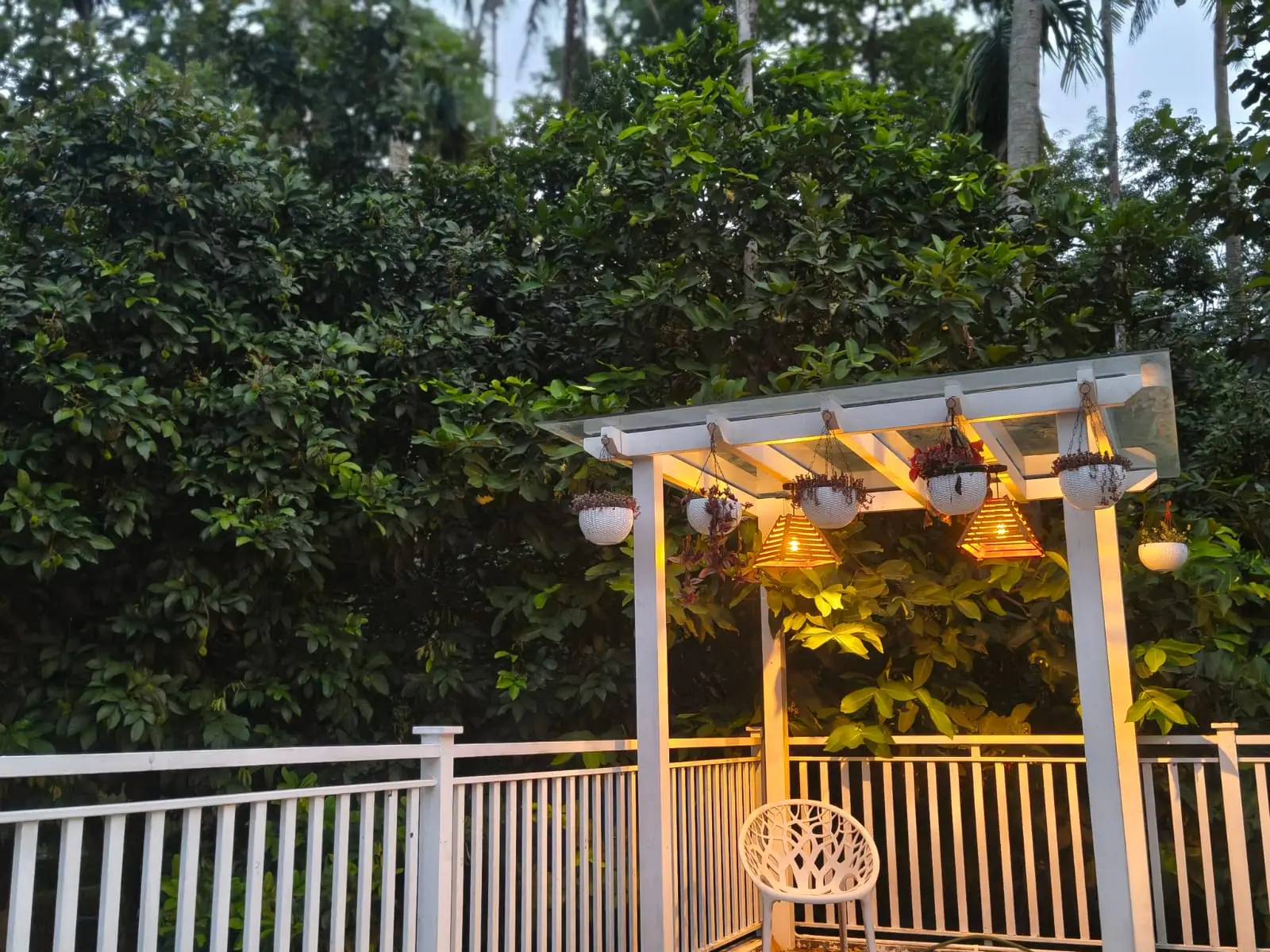 White pergola on the upper deck of Nyra Thottam with hanging planters and warm lanterns at dusk