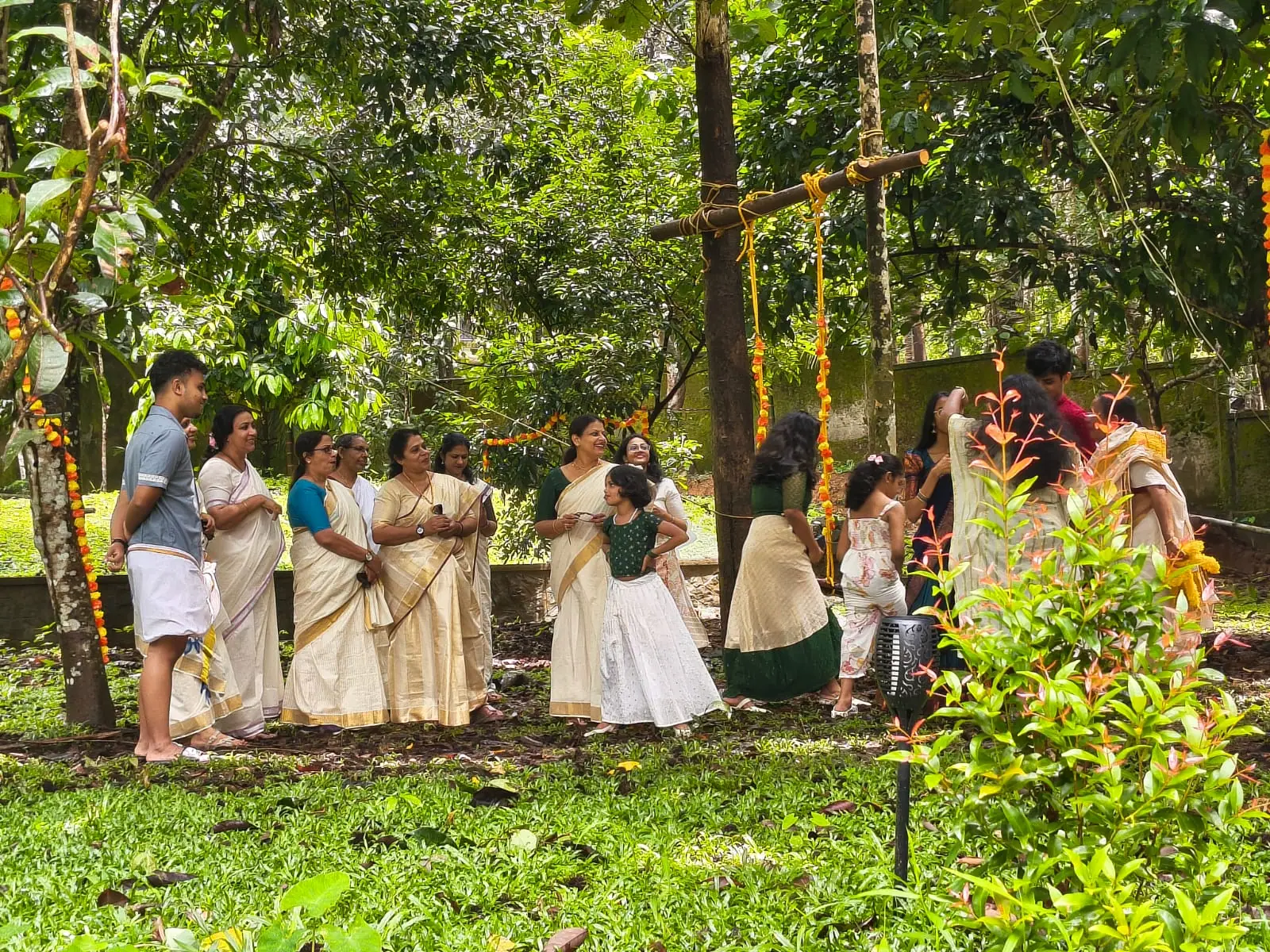 Family gathered under the trees in Nyra Thottam's garden beside a traditional swing decorated with marigold garlands